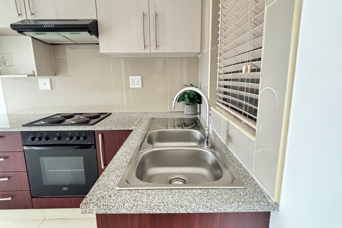 A clean, modern kitchen featuring granite countertops, stainless steel sink, built-in oven, electric hob, and neutral cabinetry with tiled splashbacks.