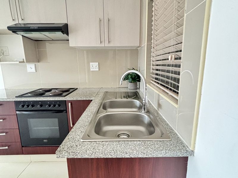 A clean, modern kitchen featuring granite countertops, stainless steel sink, built-in oven, electric hob, and neutral cabinetry with tiled splashbacks.