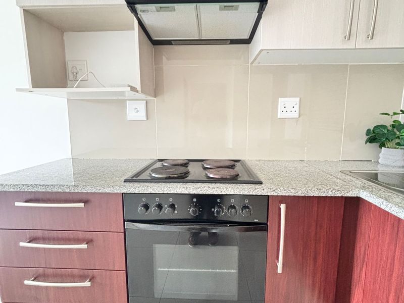 A modern kitchen featuring granite countertops, two-tone cabinetry, a built-in oven, electric hob, and an extractor fan.