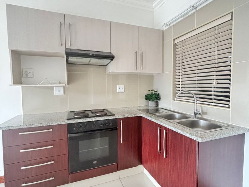 A clean, functional kitchen featuring two-tone cabinetry, granite countertops, a built-in oven with hob, and a stainless steel double sink.