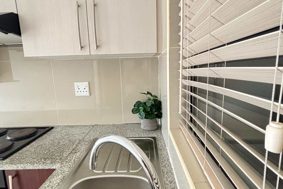 A clean and functional kitchen area featuring granite countertops, a stainless steel sink with a chrome mixer tap, and modern built-in cabinetry.