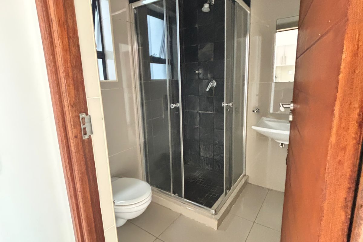 A compact bathroom featuring a glass shower enclosure, wall-mounted basin, toilet, and neutral floor tiling with a dark tiled shower feature wall.