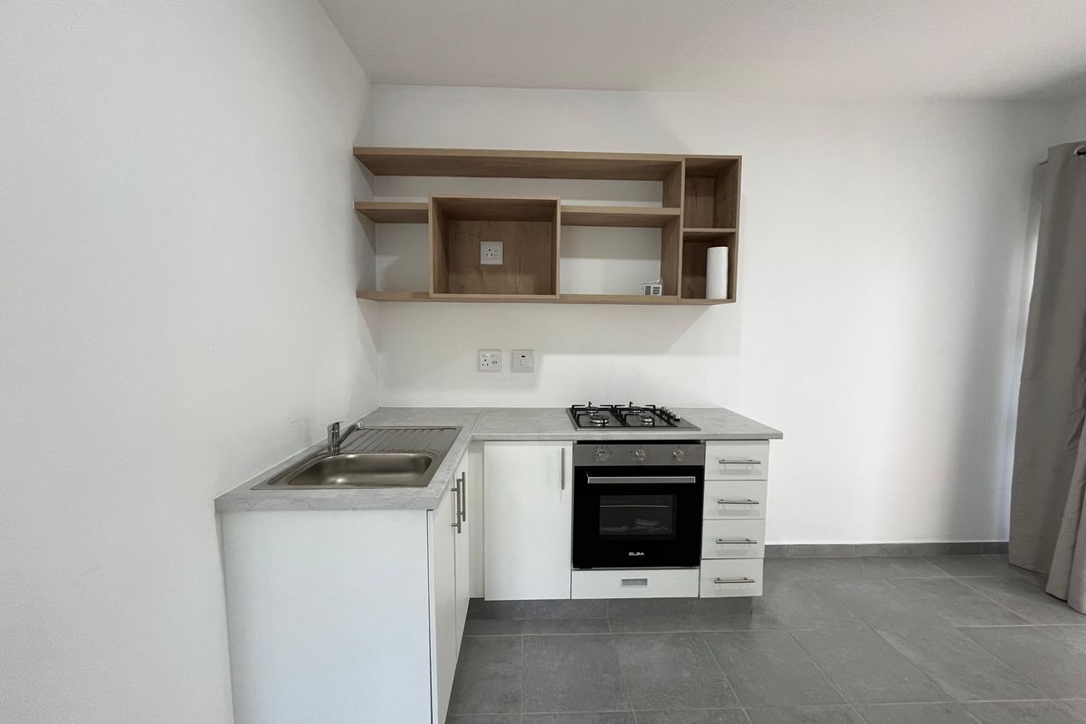 A clean, modern kitchen featuring white cabinetry, light wood open shelving, a built-in oven with gas hob, and grey tiled flooring.