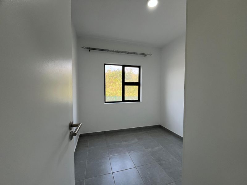 A clean, empty bedroom featuring neutral grey floor tiles, white walls, and an aluminium-framed window with a fitted curtain rod.
