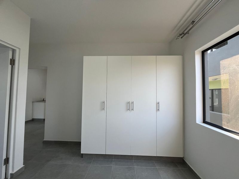 A clean, modern bedroom featuring neutral tiled flooring, a large built-in wardrobe, and a window with a curtain track.