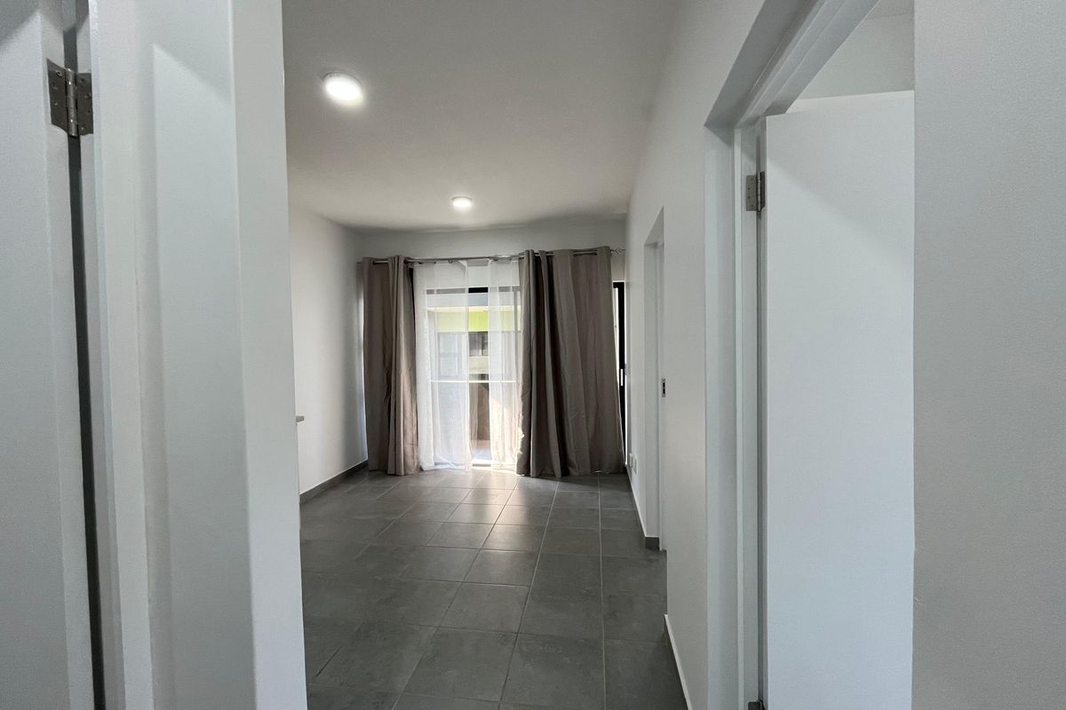 A bright, empty living area featuring neutral tiled flooring, recessed lighting, and a sliding glass door leading to an outdoor space.