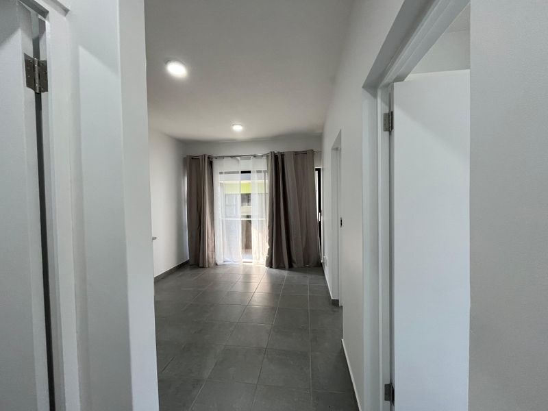 A bright, empty living area featuring neutral tiled flooring, recessed lighting, and a sliding glass door leading to an outdoor space.