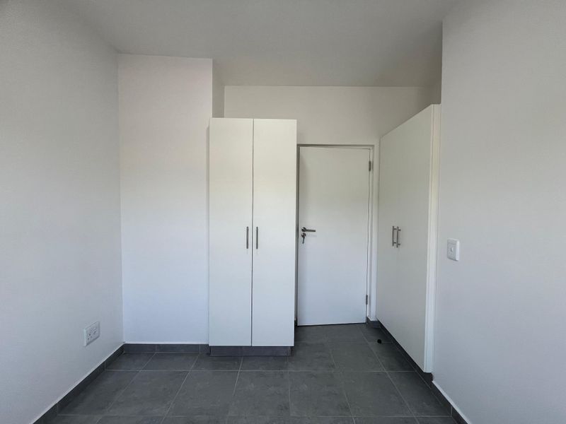 A clean, empty bedroom featuring neutral tiled flooring and white built-in cupboards, offering a blank canvas for personalization.