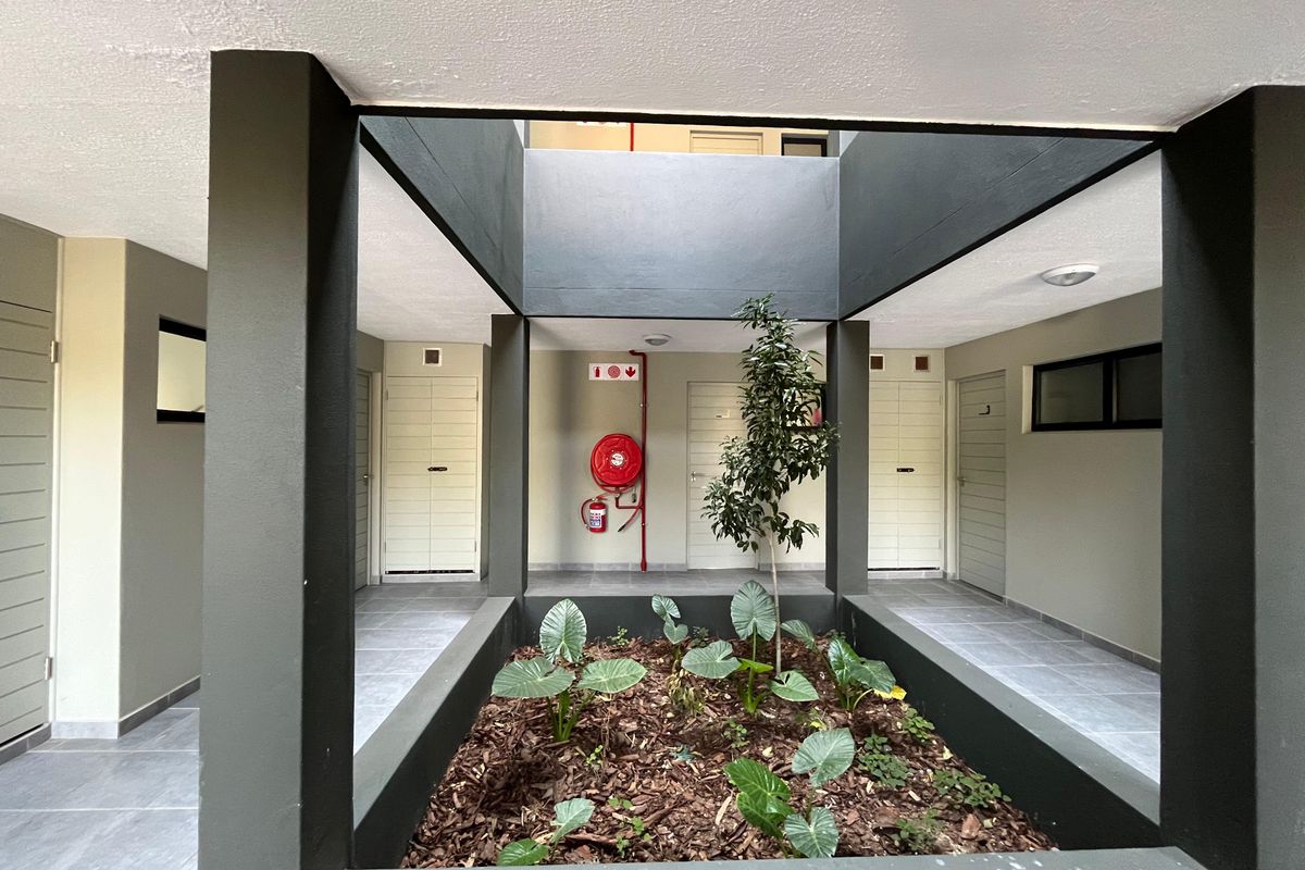 A modern, well-maintained apartment complex central courtyard featuring tiled walkways, a landscaped garden bed, and integrated fire safety equipment.