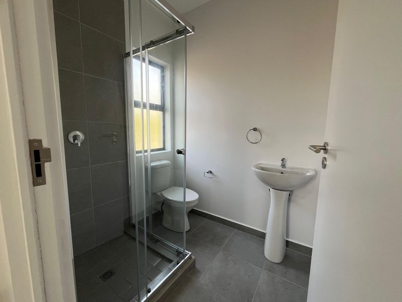 A clean and modern bathroom featuring a pedestal basin, a toilet, and a glass-enclosed shower with grey floor and wall tiling.