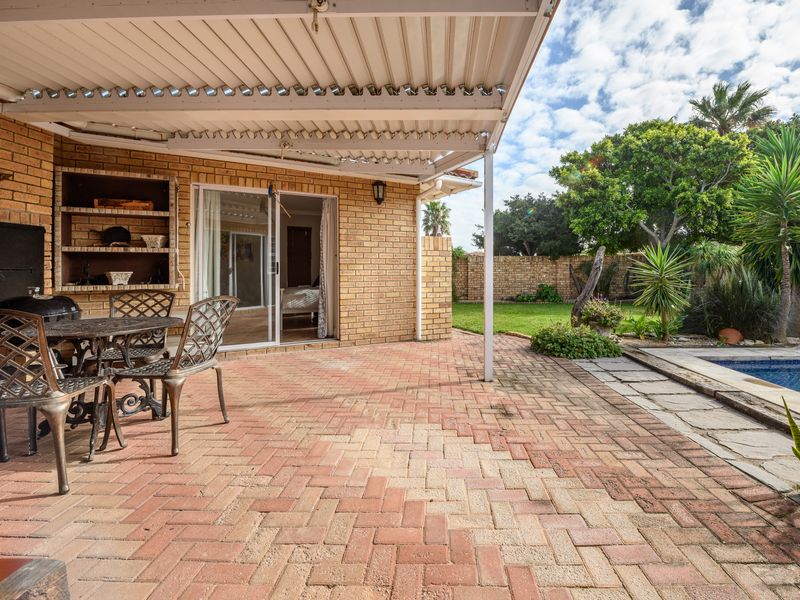 Covered brick-paved patio featuring a built-in braai, overlooking a private swimming pool and landscaped garden area.