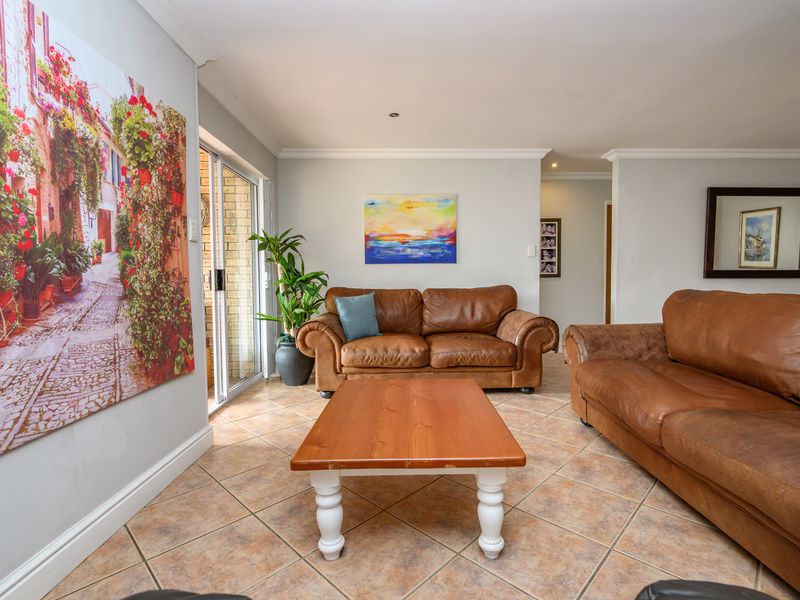 A well-lit living room featuring neutral tiled flooring, coved ceiling cornices, and a sliding glass door providing access to the outdoor area.