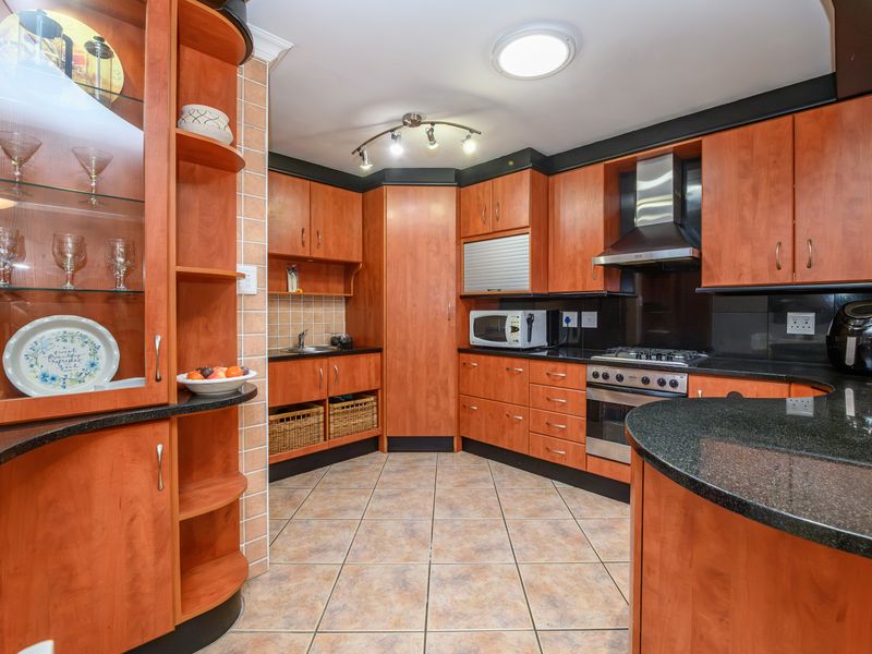 A functional kitchen featuring warm-toned wooden cabinetry, granite countertops, a gas hob with extractor fan, and tiled flooring throughout.