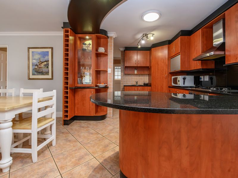 Open-plan kitchen and dining area featuring warm-toned wooden cabinetry, granite countertops, tiled flooring, and integrated storage solutions.