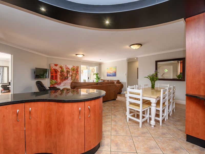 Spacious open-plan living and dining area featuring a kitchen with granite countertops, cherry wood cabinetry, and a distinctive curved bulkhead ceiling design.