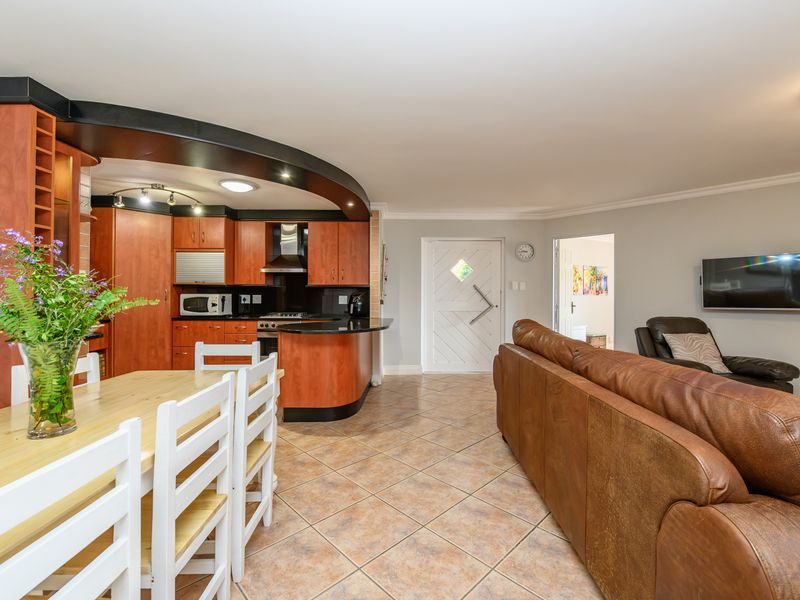 Open-plan living and kitchen area featuring warm-toned cabinetry, tiled flooring, and a functional layout connecting the dining space to the main living zone.