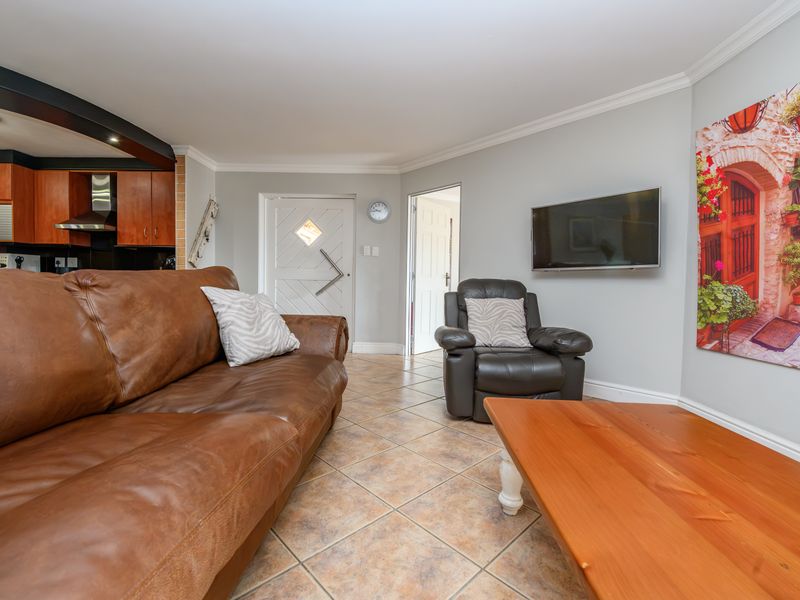 Open plan living area featuring tiled flooring, crown molding, and an integrated kitchen space with wooden cabinetry.