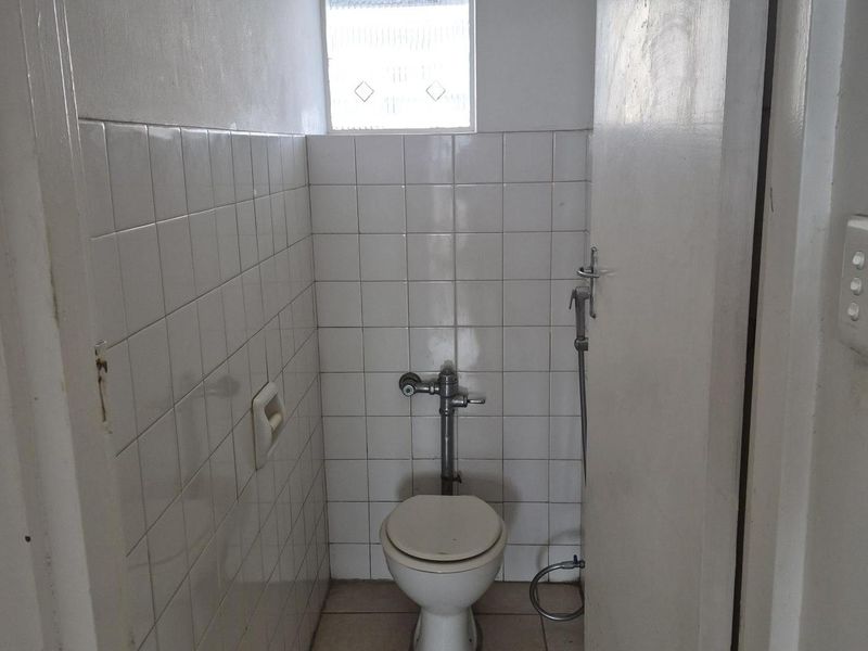 A compact, functional bathroom featuring white wall tiles, tiled flooring, a standard toilet, and a bidet spray attachment.