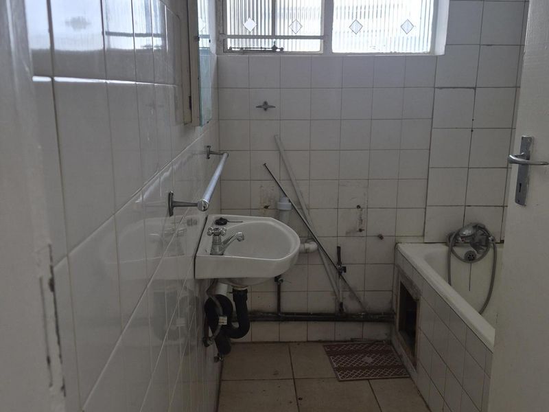 A dated bathroom featuring a wall-mounted basin, bathtub, and tiled finishes, currently requiring significant renovation and repair to modernize the space.