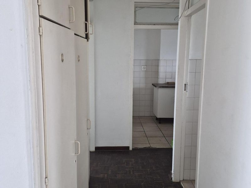 A functional hallway featuring built-in storage cupboards and parquet flooring, leading through to a tiled kitchen area.