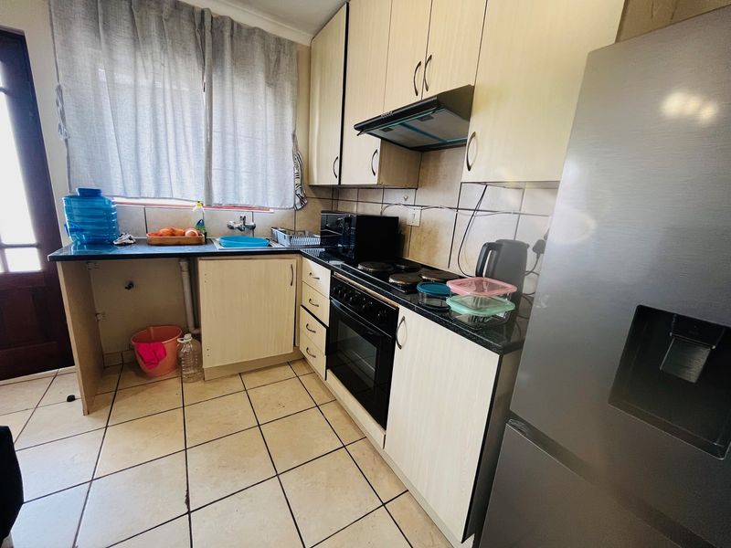 Compact kitchen featuring light-toned cabinetry, dark countertops, built-in oven with hob, and tiled flooring, offering a functional layout for daily meal preparation.