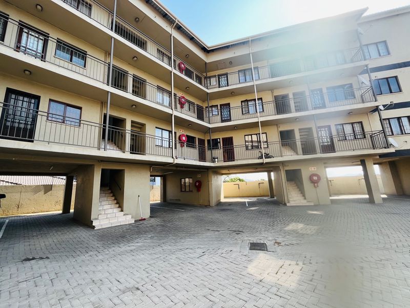 Exterior view of a multi-story apartment complex featuring paved parking, external staircases, and balcony access for individual units.