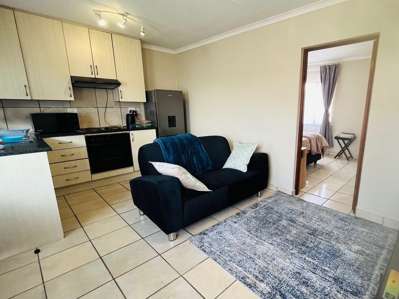 Open-plan living area featuring a compact kitchen with built-in cabinetry, oven, and extractor fan, seamlessly connected to the living space with tiled flooring.