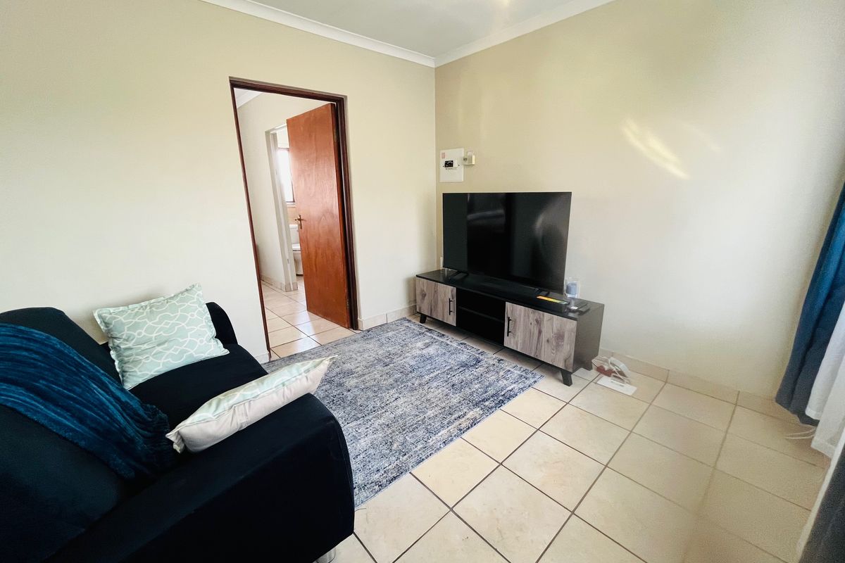 A living room featuring neutral wall paint, tiled flooring, and a coved ceiling, with an adjacent doorway leading to a bathroom area.