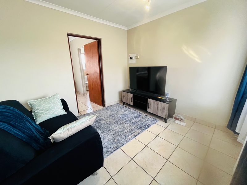 A living room featuring neutral wall paint, tiled flooring, and a coved ceiling, with an adjacent doorway leading to a bathroom area.
