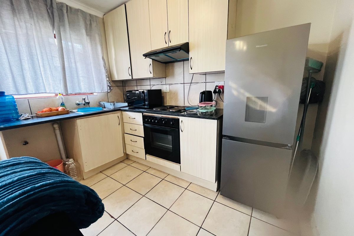 A functional kitchen featuring light-toned built-in cabinetry, a built-in oven with extractor fan, tiled backsplash, and ceramic floor tiles.