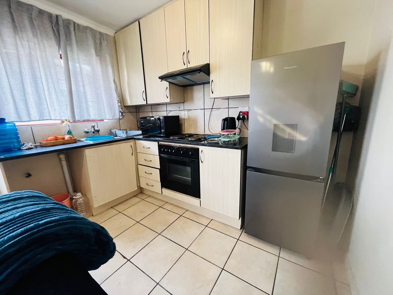 A functional kitchen featuring light-toned built-in cabinetry, a built-in oven with extractor fan, tiled backsplash, and ceramic floor tiles.