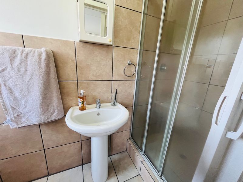 A functional bathroom featuring a pedestal basin, tiled walls, and a glass-enclosed shower unit.