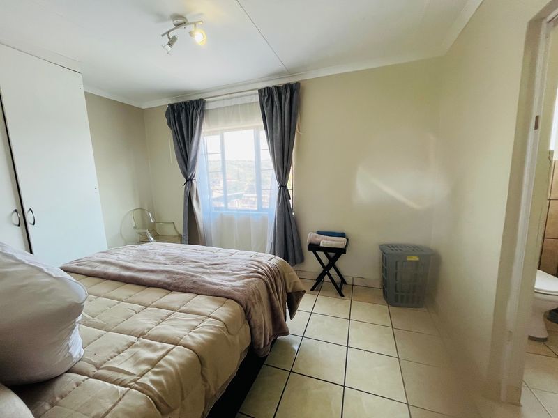 A bedroom featuring tiled flooring, a built-in wardrobe, and a window with curtains, with an adjacent en-suite bathroom visible.