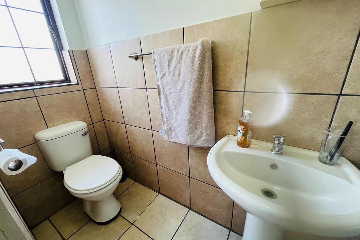 A functional bathroom featuring a pedestal basin, toilet, and neutral wall and floor tiling.