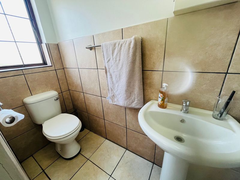 A functional bathroom featuring a pedestal basin, toilet, and neutral wall and floor tiling.