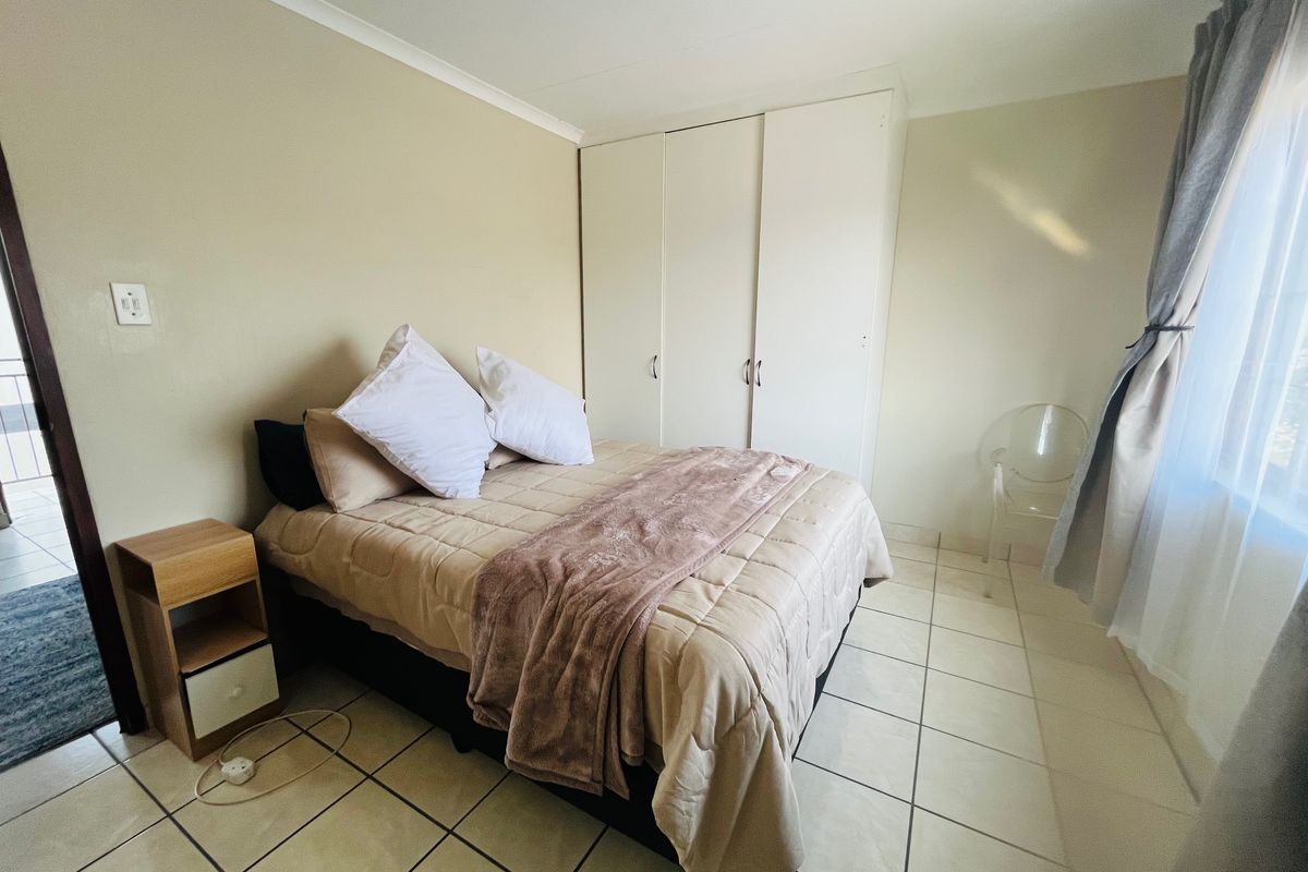 A functional bedroom featuring neutral wall tones, tiled flooring, and a built-in wardrobe providing ample storage space.