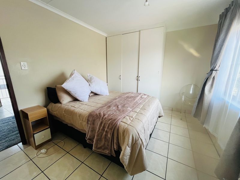 A functional bedroom featuring neutral wall tones, tiled flooring, and a built-in wardrobe providing ample storage space.