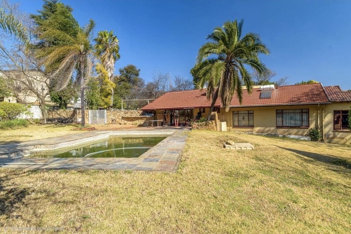 Rear exterior view of the house featuring a swimming pool, stone paving, and a large garden area with mature trees.