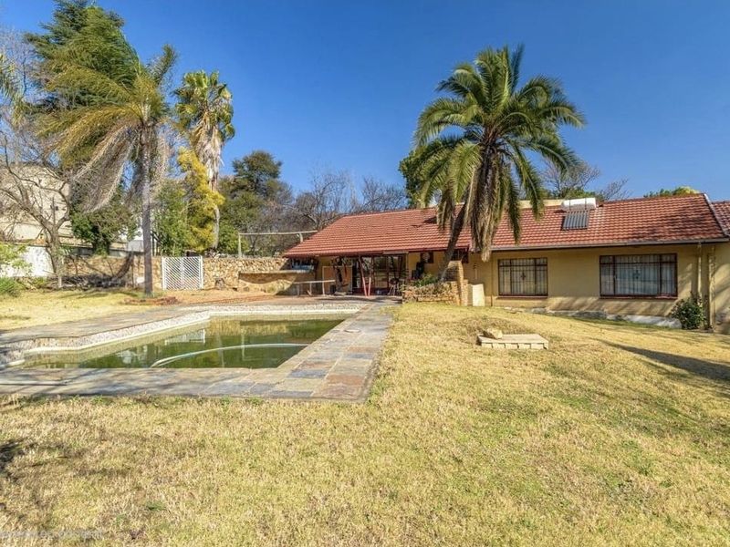 Rear exterior view of the house featuring a swimming pool, stone paving, and a large garden area with mature trees.