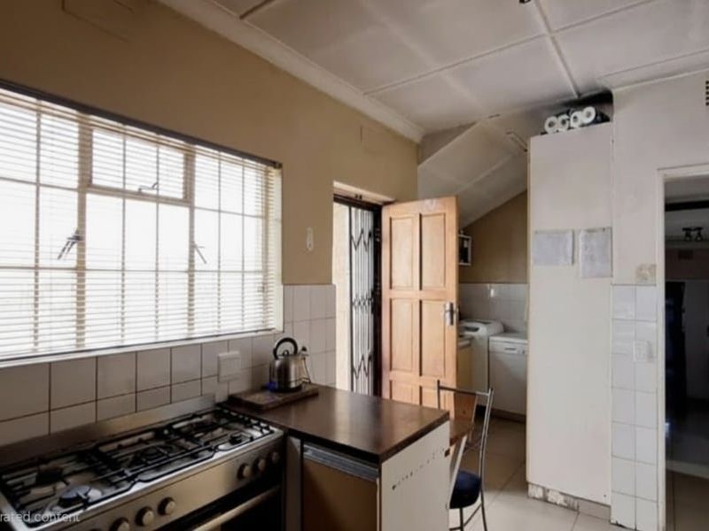 A functional kitchen featuring a gas stove, tiled splashbacks, and built-in cabinetry, with direct access to an exterior security gate.