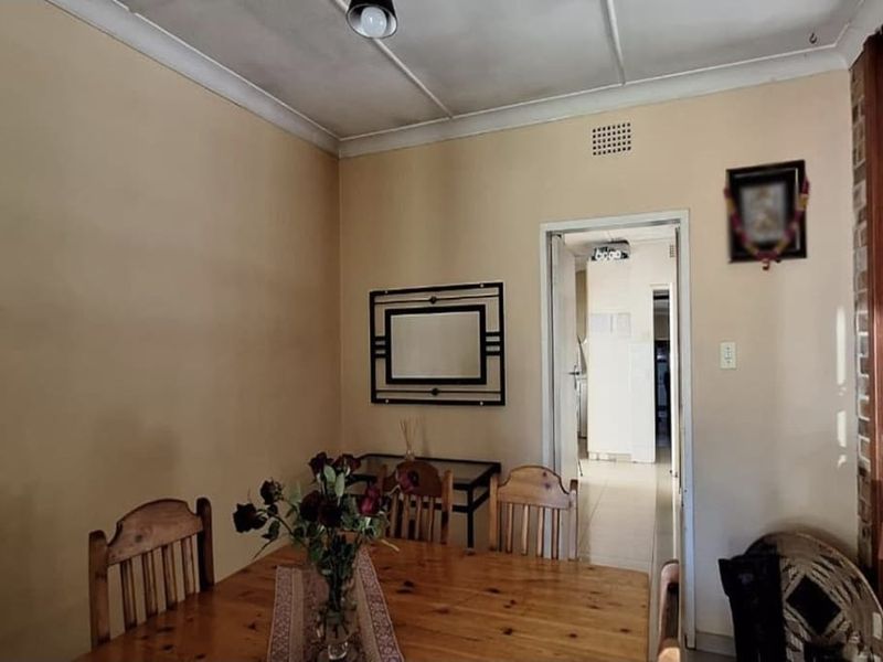 A dining area featuring cove cornicing and a central ceiling light, providing access to an adjacent hallway.