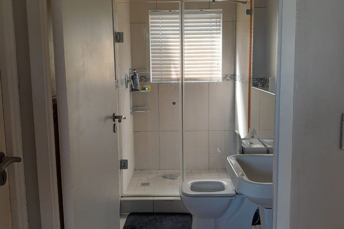 A compact bathroom featuring a glass-enclosed shower, pedestal basin, and toilet with neutral wall and floor tiling.