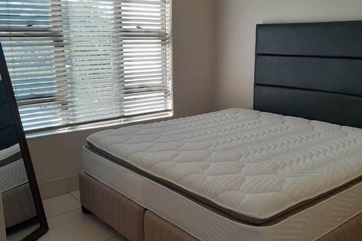 A bedroom featuring neutral walls, tiled flooring, and a window fitted with venetian blinds and a curtain rod.