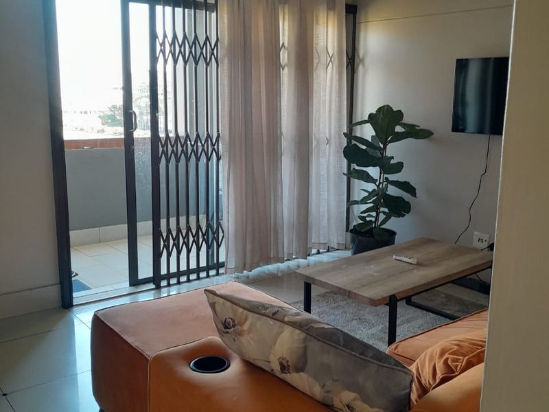 A living room featuring tiled flooring and a sliding glass door with a security gate, providing access to an outdoor balcony area.