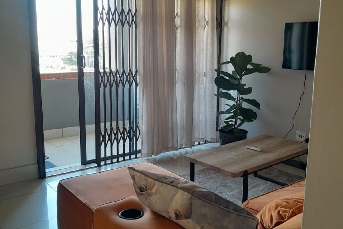 A living room featuring tiled flooring and a sliding glass door with a security gate, providing access to an outdoor balcony area.