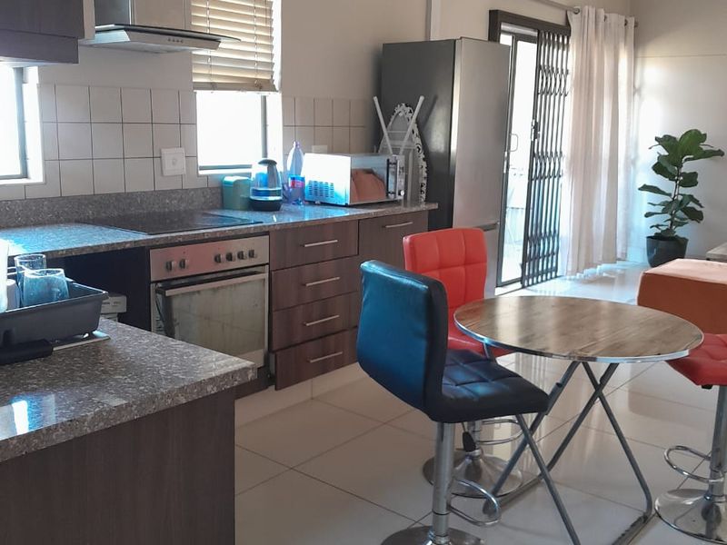Open-plan kitchen and dining area featuring modern cabinetry, granite countertops, built-in oven and hob, tiled floors, and direct access to a patio.