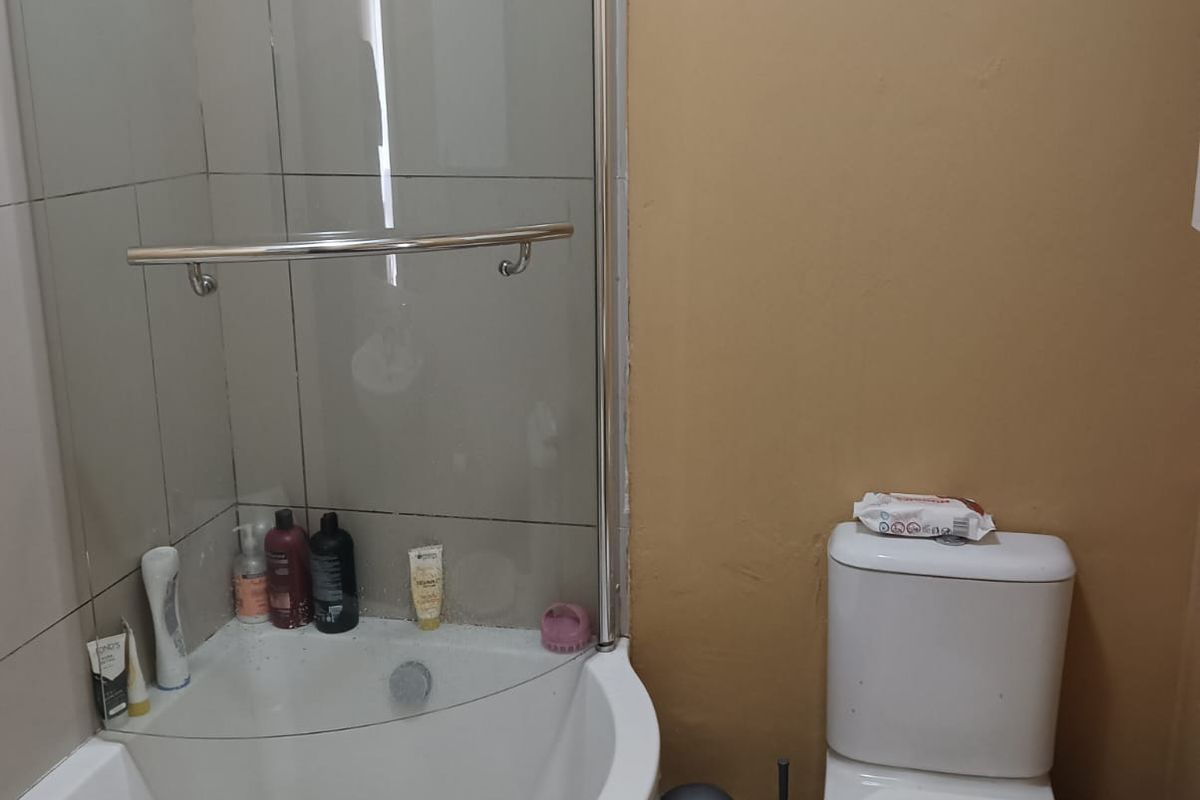 Compact bathroom featuring a corner shower enclosure, standard toilet, and wash basin, requiring cosmetic updates to the wall finishes.