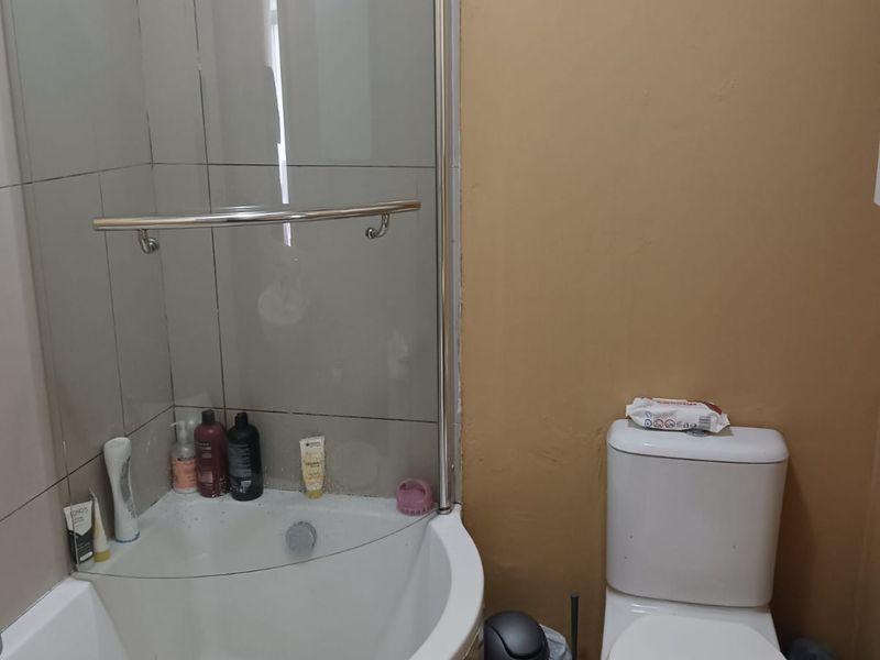 Compact bathroom featuring a corner shower enclosure, standard toilet, and wash basin, requiring cosmetic updates to the wall finishes.
