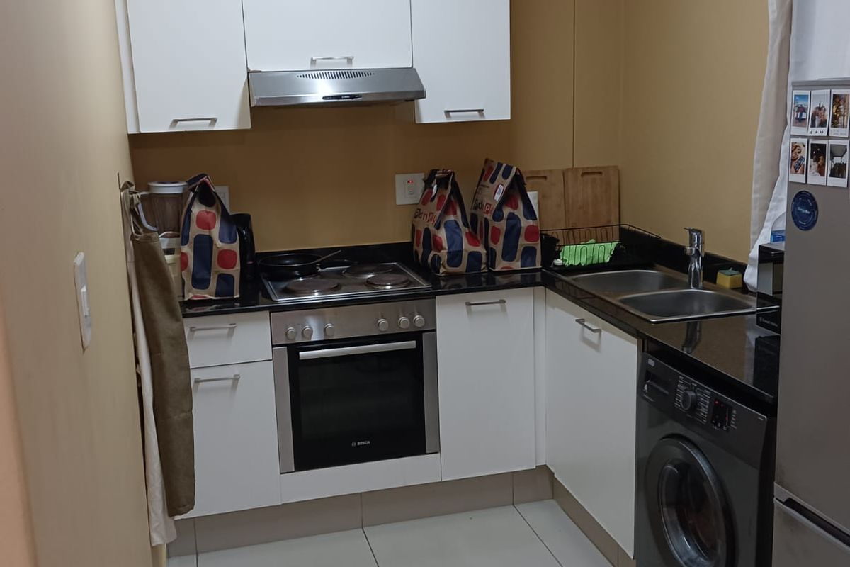 Compact kitchen featuring white cabinetry, granite countertops, built-in oven, electric hob, extractor fan, and tiled flooring.