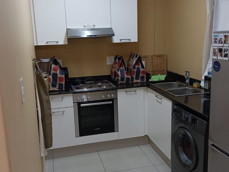 Compact kitchen featuring white cabinetry, granite countertops, built-in oven, electric hob, extractor fan, and tiled flooring.
